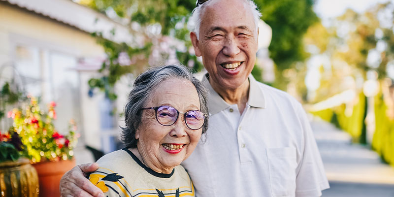 Senior Asian couple outdoors smiling at camera.